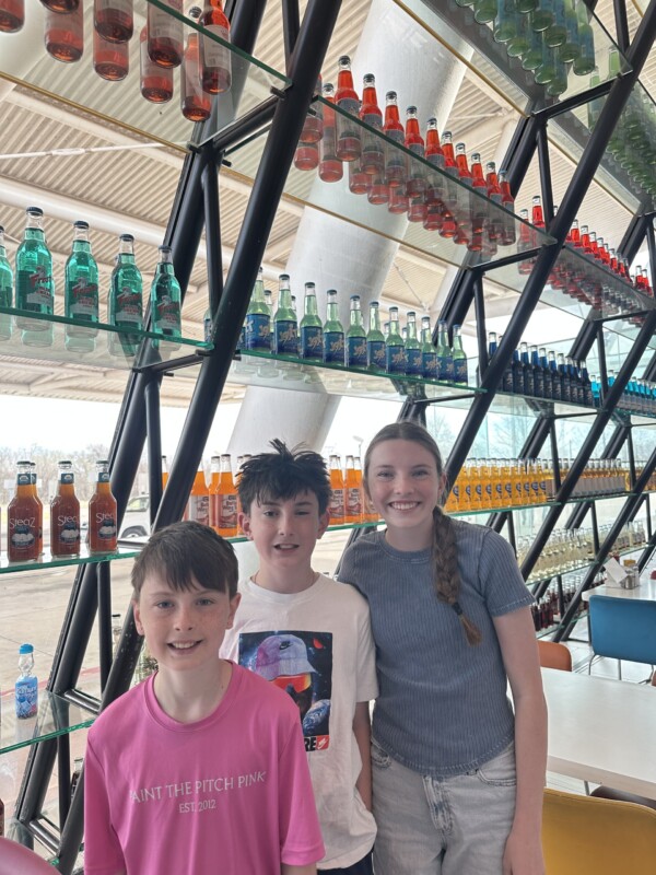 three kids in front of colorful soda bottles at pops 